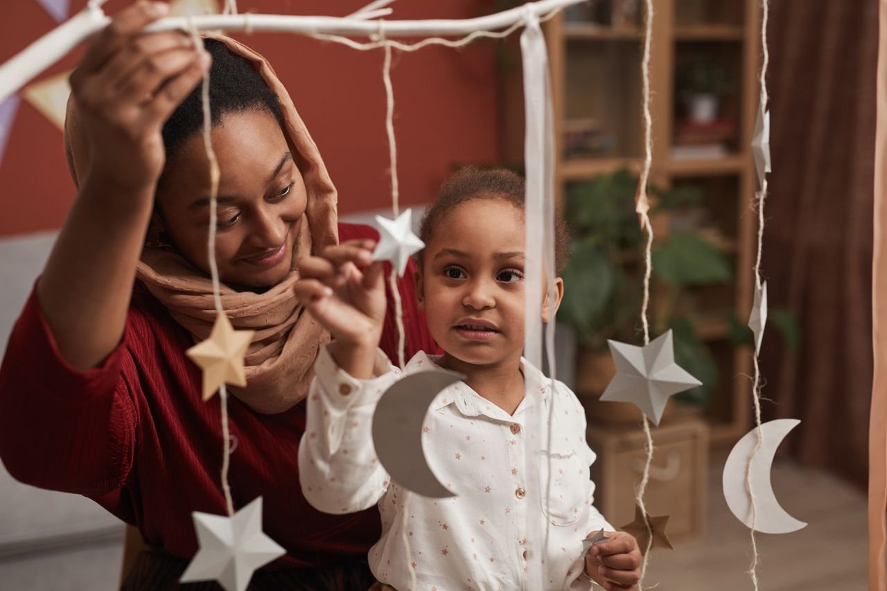 A mother and daughter enjoy bonding indoors while creating handmade star and moon decorations.